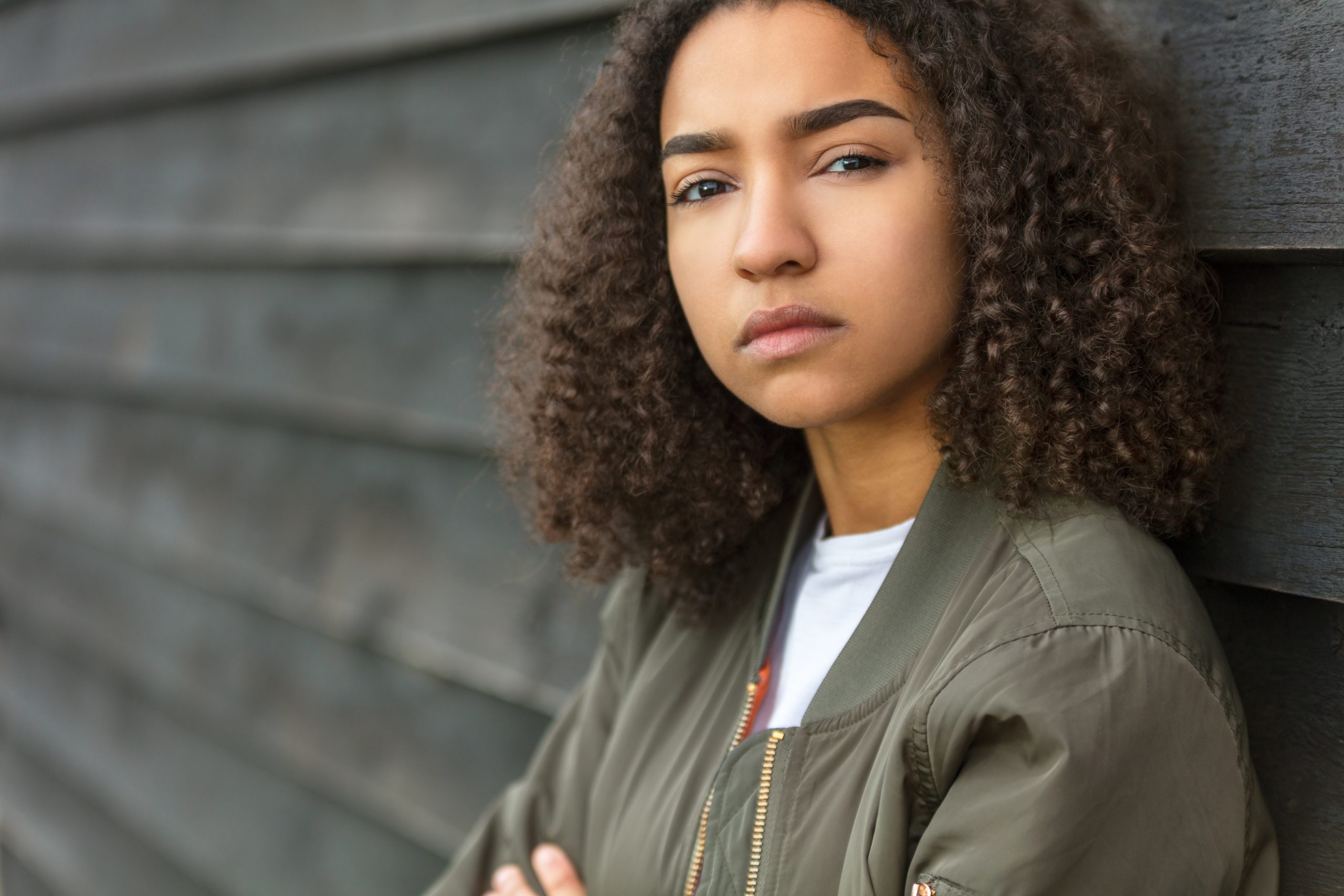 Girl with curly hair leaning against a wall.